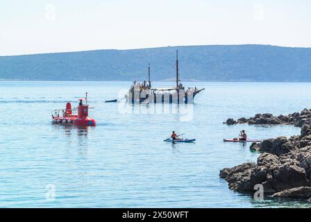 krk, kroatien, 30. april 2024, historisches Holzschiff, halb-U-Boot mit Glasboden und Stehpaddler in einer Bucht *** krk, kroatien, 30. april 2024, historisches holzschiff, halb-unterseeisches Glasbodenboot und Stand Up Paddler in einer bucht Copyright: xx Stockfoto