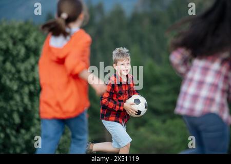 Junge Schüler spielen mit dem Lehrer im Freien, in der Natur, während des Feldunterrichts, laufen mit Ball. Engagierte Lehrer während der Aktivitäten im Freien Stockfoto