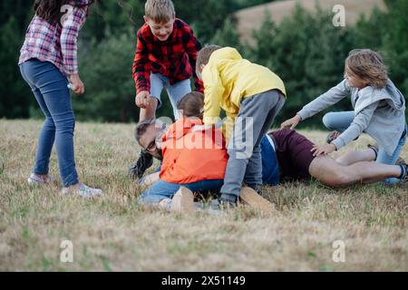 Junge Schüler spielen mit dem Lehrer im Freien, in der Natur, während des Feldunterrichts, laufen mit Ball. Engagierte Lehrer während der Aktivitäten im Freien Stockfoto