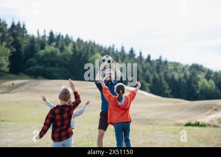 Junge Schüler spielen mit dem Lehrer im Freien, in der Natur, während des Feldunterrichts, laufen mit Ball. Engagierte Lehrer während der Aktivitäten im Freien Stockfoto