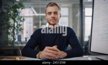 Blickwinkel von der Kamera aus, während ein junger Projektmanager in einer kreativen Büroumgebung einen Videoanruf führt. Glücklicher kaukasischer männlicher Spezialist, der mit einem Kollegen über eine Live-Kamera spricht. Stockfoto