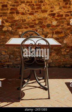 Ein Tisch mit zwei Stühlen in der Sonne auf der Hauptstraße der Altstadt von Certaldo - Certaldo Alto - in der Nähe von Florenz in der Toskana, Italien. Mit Ziegelwänden. Stockfoto