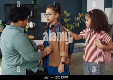 Seitliches Porträt der schwarzen Seniorin, die Mädchen mit Rucksack für die Schulvorbereitungen hilft Stockfoto