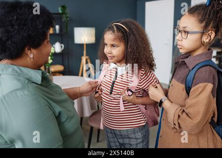 Porträt eines kleinen afroamerikanischen Mädchens mit Rucksack, das morgens mit der Hilfe von Großmutter für die Schule bereit ist Stockfoto