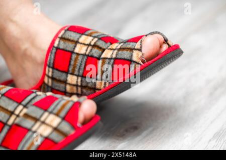 Ein Fuß in einen alten, undichten Slipper. Alter Pantoffel. Sneaker mit Lochmuster. Die Spitze ragt aus dem Schuh im Slipper heraus Stockfoto