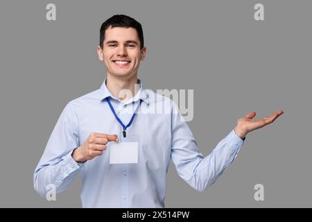 Lächelnder Mann mit leerem Abzeichen, der etwas auf grauem Hintergrund zeigt Stockfoto