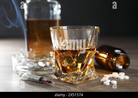 Alkohol- und Drogensucht. Whiskey in Glas, Spritze, Pillen und Zigaretten auf Holztisch Stockfoto