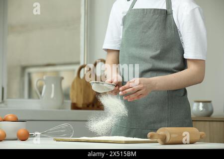 Frau siebt Mehl am Tisch in der Küche, Nahaufnahme. Leerzeichen für Text Stockfoto