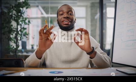 Point of View von der Kamera aus mit Young Black Project Manager, der ein Videoanruf in einer kreativen Büroumgebung führt. Glücklicher afroamerikanischer männlicher Spezialist zeigt dem Kollegen die OK-Geste über Live-Kamera. Stockfoto