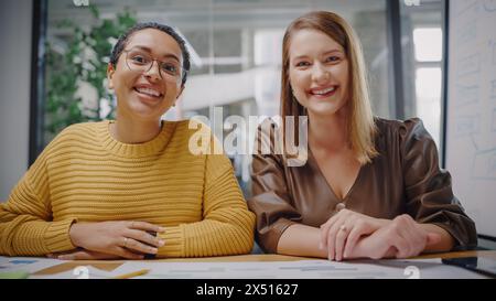 Porträt von zwei verschiedenen Projektmanagern, die Videoanrufe in einer kreativen Büroumgebung tätigen. Glückliche Weibchen, Kaukasier und Lateinspezialisten, die Kollegen über Live Camera zuhören. Stockfoto