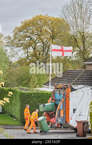 Recyclingarbeiter in orangefarbenen Jacken und Hosen laden am St. George's Day Müll aus grünen Mülltonnen in einen zerbrechenden Lastwagen. Stockfoto