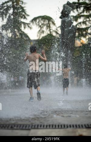 Fröhliche, zufriedene und verspielte Kinder, die sich im Brunnen der Stadt abkühlen und vor der Hitze des Sommertages entfliehen. Stockfoto