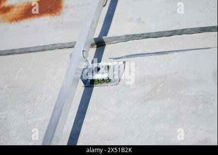 Nahaufnahme der Metallhalterung zur Montage von Solarpaneelen auf Flachdach. Halterung mit gut sichtbaren Schrauben am Dach befestigt, die die ersten Schritte bei der Installation von Solarmodulen demonstrieren. Stockfoto