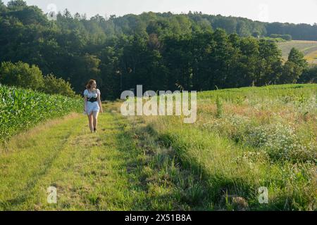 Eine hübsche junge Frau, die ein weißes, kurzes Kleid trägt, in grüner Natur vorwärts rennt Stockfoto