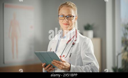 Porträt einer erfahrenen Ärztin mit weißem Mantel, die in ihrem Büro am Tablet-Computer arbeitet. Medizinischer Arzt oder Oberschwester schaut auf die Kamera und lächelt sanft. Stockfoto