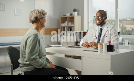 Afroamerikanischer Familienarzt verschreibt Medikamente für ältere weibliche Patienten und spricht mit ihr während der Konsultation in einer Gesundheitsklinik. Arzt sitzt hinter einem Schreibtisch im Krankenhausbüro. Stockfoto