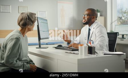Afroamerikanischer Familienarzt verschreibt Medikamente für ältere weibliche Patienten und spricht mit ihr während der Konsultation in einer Gesundheitsklinik. Arzt sitzt hinter einem Schreibtisch im Krankenhausbüro. Stockfoto