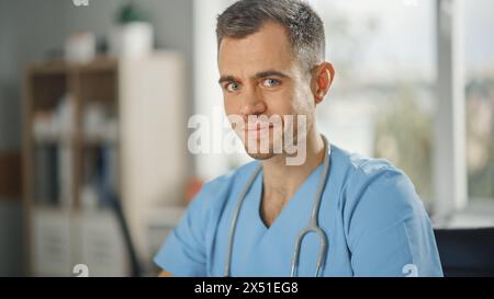 Porträt einer erfahrenen männlichen Krankenschwester in blauer Uniform, die in der Arztpraxis in die Kamera lächelt. Medizinische Fachkraft arbeitet an der Bekämpfung von Stereotypen zur Geschlechtervielfalt in der Pflegekarriere. Stockfoto