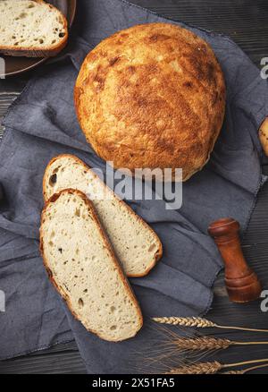 Frisch gebackenes, handwerkliches Brot mit Scheiben und Weizenohren auf hölzernem Hintergrund Stockfoto