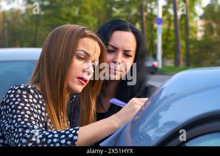 Eine junge Frau mit ihrem Freund, die ein Dokument auf dem Kofferraum eines Autos unterschreibt Stockfoto