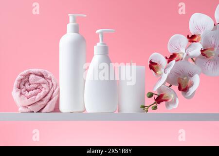 Kosmetikflaschen, Handtuch, Orchidee und Kerze im Badezimmer. Weißer Flakon, Seifenspender und andere Toilettenartikel für die persönliche Hygiene. Kunststoffbehälter Stockfoto