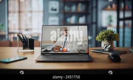 Laptop-Computer mit Videoanruf an einen männlichen Arzt, der auf dem Tisch im gemütlichen Wohnzimmer steht. Im Hintergrund stilvolles modernes helles Home Office Studio tagsüber mit großem Stadtfenster. Stockfoto