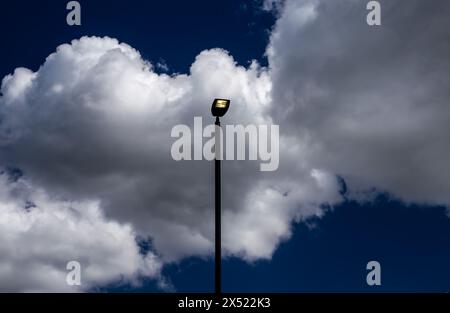 LED-Leuchten leuchten tagsüber mit dramatischem blauem Himmel und weißen Wolken. Hohe Lampenständer stehen sowohl im hoch- als auch im Querformat aufrecht. Platz zum Kopieren Stockfoto