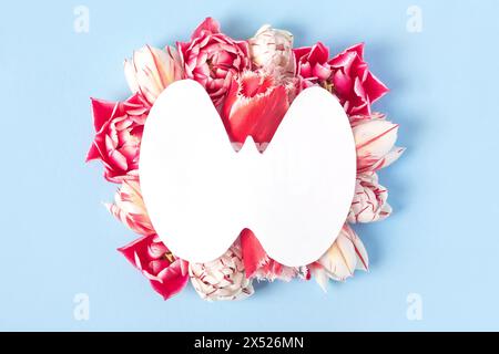 Welttag Der Schilddrüse. Konzept der Schilddrüsenerkrankung und Gesundheit. Weißbuchform der Schilddrüse auf blauem Hintergrund mit rosa und weissen Tulpen. Platz f Stockfoto