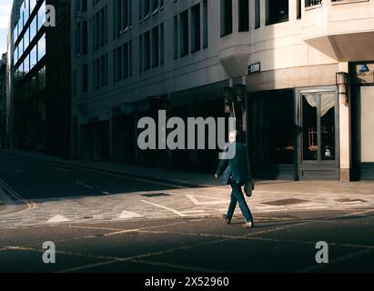 Straßenfoto eines Menschen, der über die Straße im Schacht des goldenen Sonnenlichts und der dunklen Schatten in London, Großbritannien, geht Stockfoto