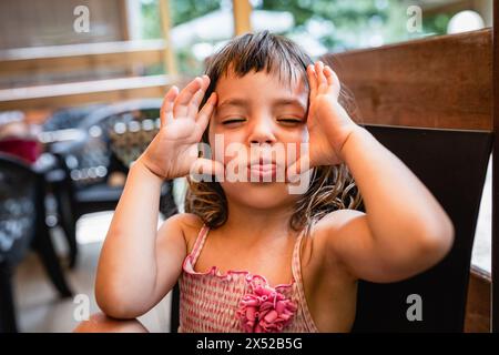 Porträt eines glücklichen kleinen Mädchens, das lustiges Gesicht macht, das draußen sitzt Stockfoto