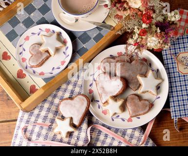Hausgemachte glasierte Herz- und sternförmige Kekse mit heißer Schokolade auf einem rustikalen Tisch. Stockfoto