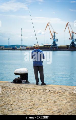 Fischer auf dem Pier mit Angelrute fängt Fische, der Blick von hinten Stockfoto