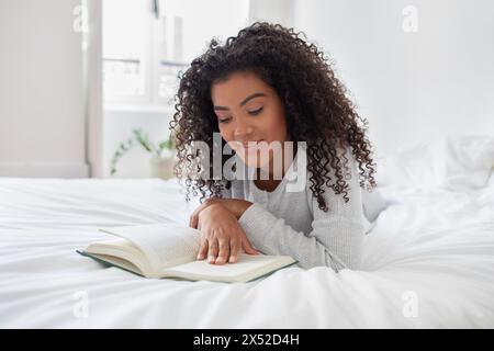 Frau, die auf dem Bett liegt und ein Buch liest Stockfoto