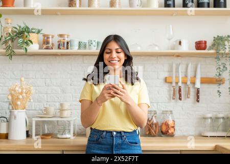 Frau, die in der Küche steht und auf das Handy schaut Stockfoto