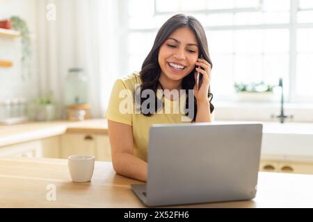 Frau, die auf dem Handy spricht, während sie einen Laptop benutzt Stockfoto