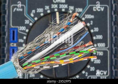 Abisoliertes Kabel mit mehreren Farben vor der Skala eines Multimeters. Multimeter misst Spannung, Strom und Widerstand. Stockfoto