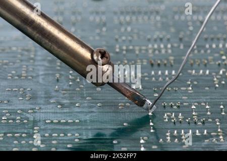 Ein Lötkolben wird vorsichtig auf der Rückseite der Leiterplatte platziert, um die Lötstellen mit dem Lötmittel zu verbinden. Stockfoto