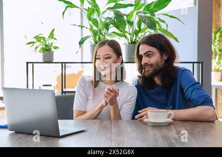 Glückliches überraschtes junges Paar, das zusammen in der Cafeteria auf den Laptop blickt Stockfoto