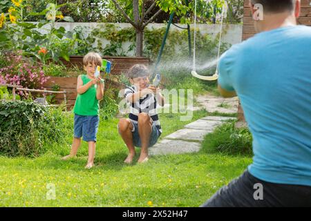Glückliche Kinder, die mit Wasserpistolen gegen ihren Vater spielen Stockfoto