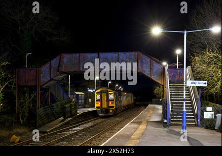 Ein Zug der Northern Rail-Klasse 158 158754 am Bahnhof Clapham, Yorkshire, auf der kleinen Nordwestlinie bei Nacht mit der Bahnhofsbrücke Stockfoto