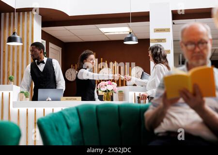 Bei der Ankunft im Luxusresort holt die pensionierte Seniorin ihre Schlüsselkarte vom Rezeptionspersonal ab und erhält Zugang zum Hotelzimmer. Frau, die den Check-in am Registrierungsschalter ausführt. Stockfoto