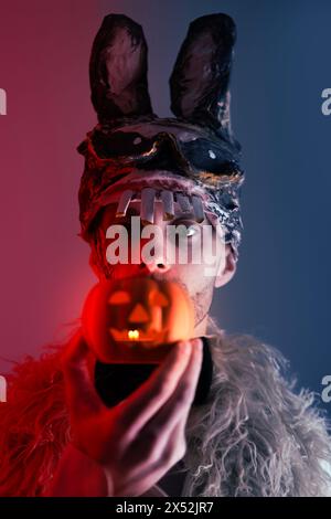 Gruseliger Hasenmann, junger Mann in einer gruseligen Hasenmaske, mit Kürbiskerzenleuchter, Thema der Angst und des Horrors in Verbindung mit Maske und Gesichtsausbrüchen Stockfoto