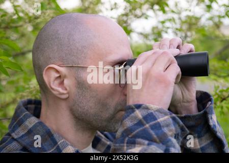 Junger Mann, versteckt in üppigem Grün, Spione bekleidet durch Ferngläser, Privatdetektiv überwacht, Nervenkitzel sucht das Ziel Stockfoto