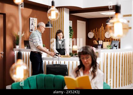 Der Rezeptionist hilft Seniorenreisenden beim Einchecken, wenn er an der Hotelrezeption ankommt. Während sich ältere Frauen im eleganten Loungebereich entspannen, hilft der Concierge männlichen Touristen bei der Unterbringung. Stockfoto