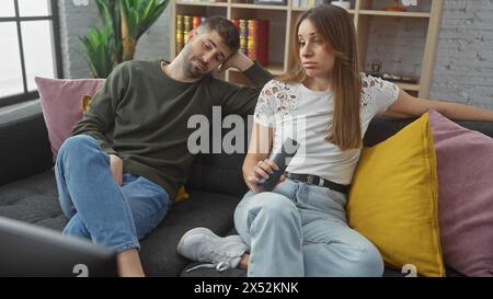 Eine desinteressierte Frau und ein Mann, der auf einem Sofa in einem modernen Wohnzimmer sitzt, zeigen Langeweile mit der Fernbedienung in der Hand. Stockfoto