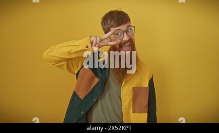 Rothaariger bärtiger Mann mit Brille, die ein Friedenszeichen vor gelbem Hintergrund macht Stockfoto