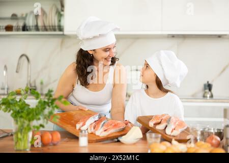 Glückliche Mutter und ihre Tochter bereiten Lachs zum Backen in der Küche vor Stockfoto