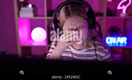 Junge gestresste Frau mit Headset in einem dunklen Spielzimmer, die müde ist oder Kopfschmerzen hat Stockfoto