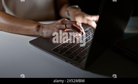 Nahaufnahme einer jungen Frau, die in einem schwach beleuchteten Raum auf einem Laptop tippt, was Professionalität und Konzentration widerspiegelt. Stockfoto