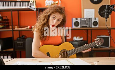 Eine junge kaukasische Frau, die in einem orangen Musikstudio Gitarre spielt und singt Stockfoto